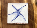 Square tile with a blue starfish design on a wooden surface. Azulejo portuguese.